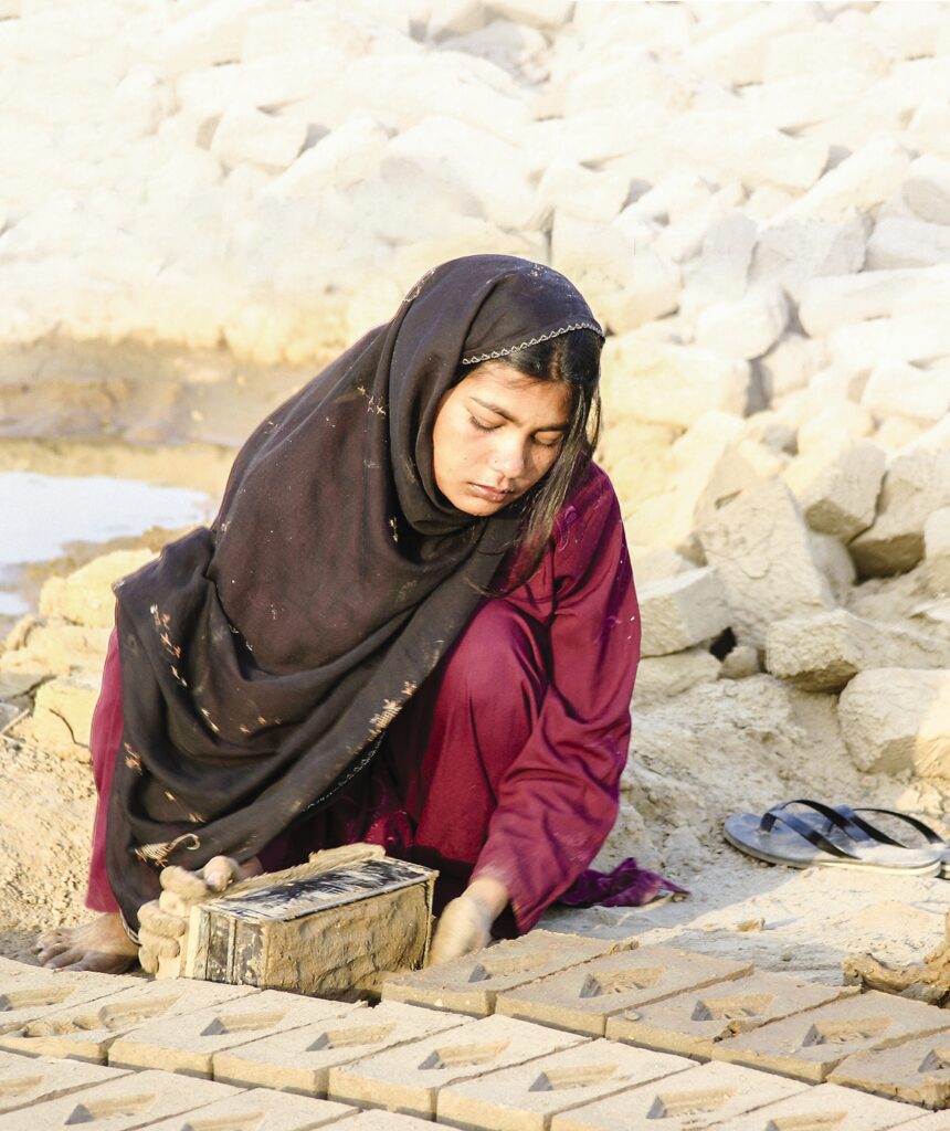 a woman sits outside and makes bricks 
